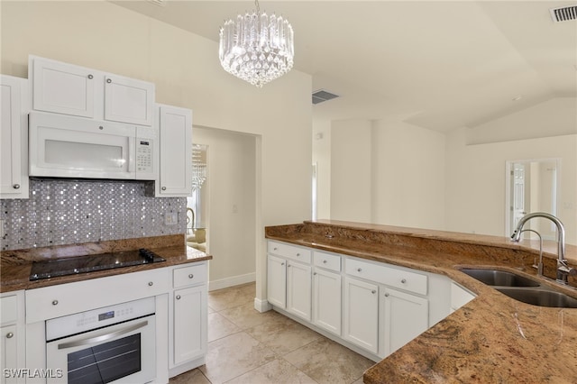 kitchen with sink, white cabinetry, hanging light fixtures, white appliances, and dark stone counters