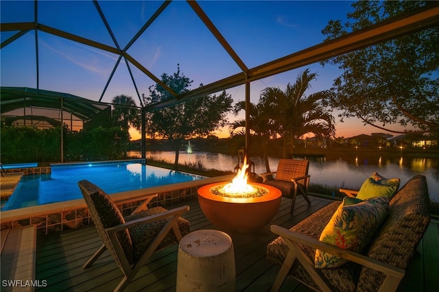 pool at dusk with a deck with water view, a lanai, pool water feature, and an outdoor fire pit