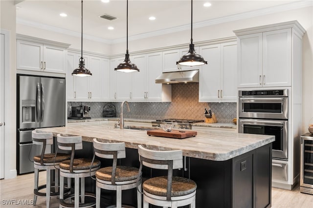 8949 Mustique Ln, Naples, FL 34114 - kitchen with appliances with stainless steel finishes, under cabinet range hood, ornamental molding, a kitchen island with sink, and hanging light fixtures