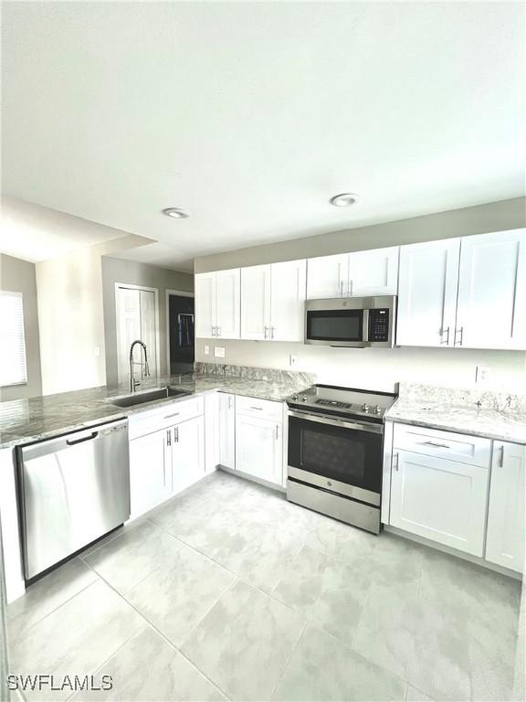 kitchen featuring sink, stone counters, appliances with stainless steel finishes, white cabinets, and kitchen peninsula