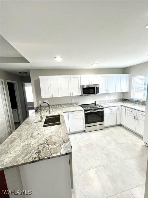 kitchen with stainless steel appliances, sink, white cabinets, and light stone counters