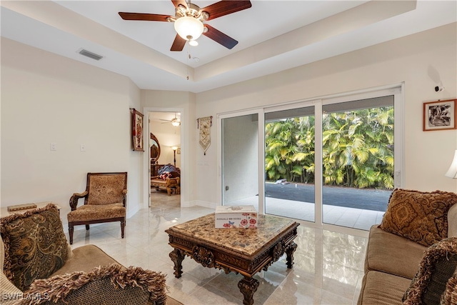 living room featuring a raised ceiling, visible vents, baseboards, and ceiling fan