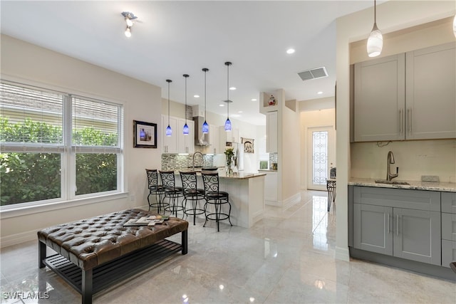 kitchen featuring sink, hanging light fixtures, gray cabinetry, and light stone counters