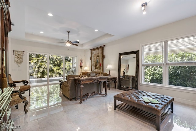 living room with a tray ceiling, ceiling fan, and a wealth of natural light