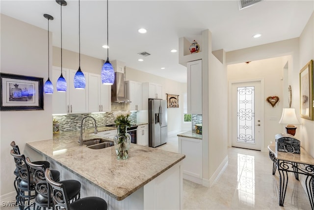 kitchen with white cabinets, wall chimney exhaust hood, stainless steel refrigerator with ice dispenser, and kitchen peninsula