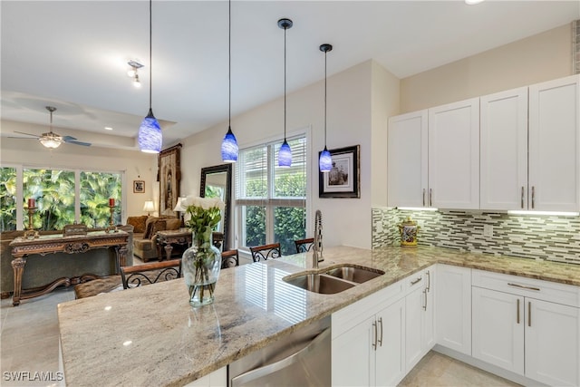 kitchen with a sink, decorative backsplash, dishwasher, white cabinets, and light stone countertops