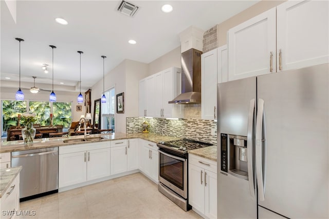 kitchen with sink, light stone counters, wall chimney range hood, stainless steel appliances, and hanging light fixtures