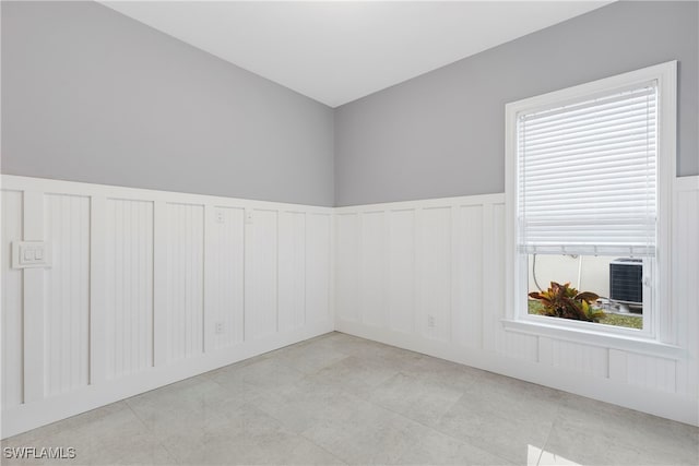 unfurnished room featuring a decorative wall, light tile patterned floors, and wainscoting