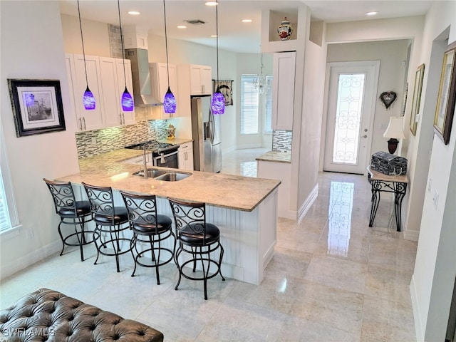 kitchen featuring wall chimney exhaust hood, appliances with stainless steel finishes, a kitchen breakfast bar, and visible vents
