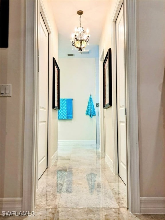 corridor featuring marble finish floor, an inviting chandelier, visible vents, and baseboards