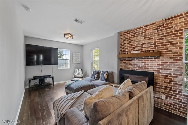 living room with a brick fireplace and dark wood-type flooring