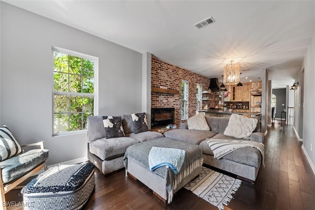 living room featuring a brick fireplace, an inviting chandelier, and dark hardwood / wood-style flooring