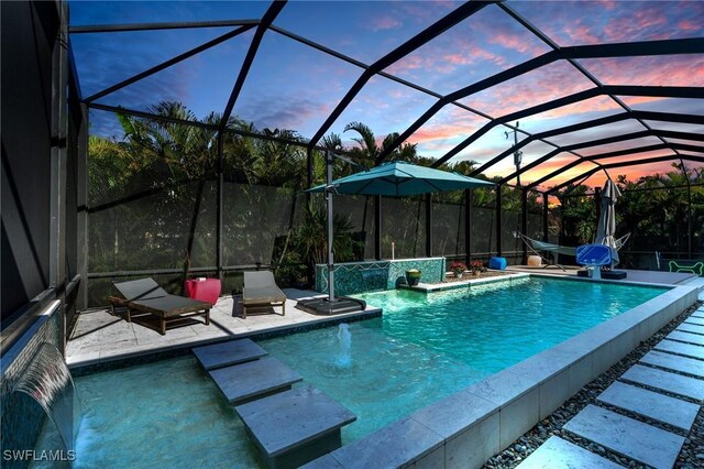 pool at dusk with a patio area, pool water feature, and glass enclosure