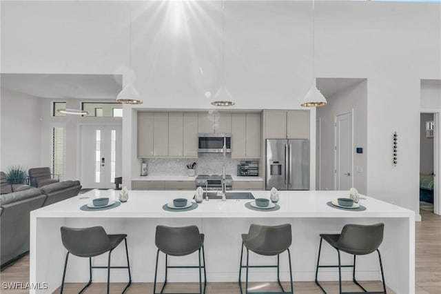 kitchen with gray cabinets, backsplash, a kitchen breakfast bar, stainless steel appliances, and light wood-type flooring