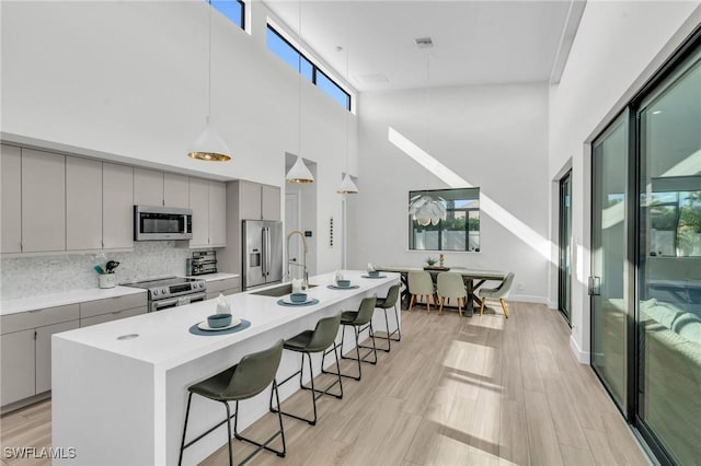 kitchen featuring appliances with stainless steel finishes, decorative light fixtures, an island with sink, sink, and gray cabinetry