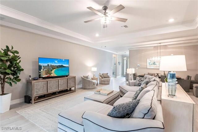 living room with a raised ceiling, crown molding, ceiling fan with notable chandelier, and light hardwood / wood-style flooring