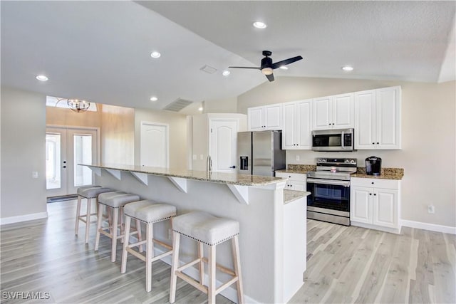 kitchen with white cabinetry, a center island with sink, appliances with stainless steel finishes, a kitchen breakfast bar, and light stone countertops