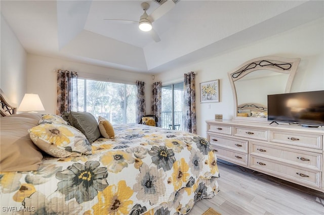 bedroom with access to exterior, a tray ceiling, ceiling fan, and light wood-type flooring