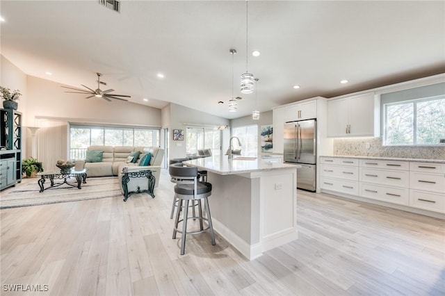 kitchen featuring pendant lighting, sink, white cabinets, stainless steel built in fridge, and a center island with sink