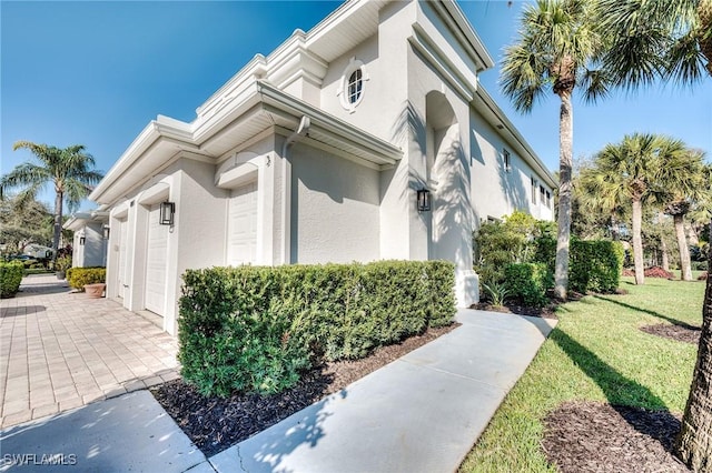 view of property exterior with a garage, decorative driveway, a lawn, and stucco siding