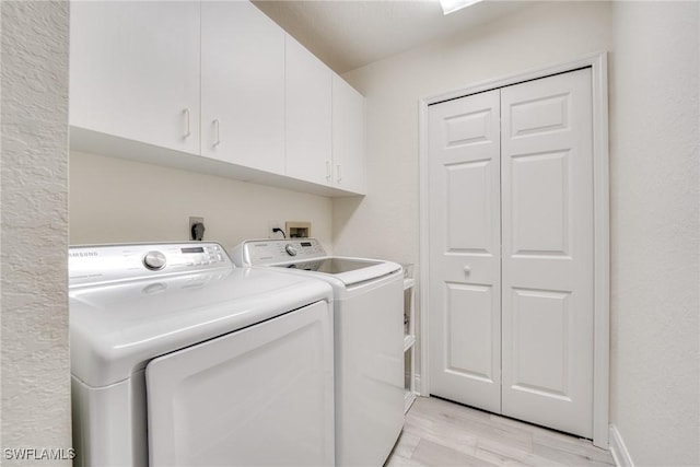 clothes washing area featuring light wood-type flooring, cabinet space, independent washer and dryer, and baseboards