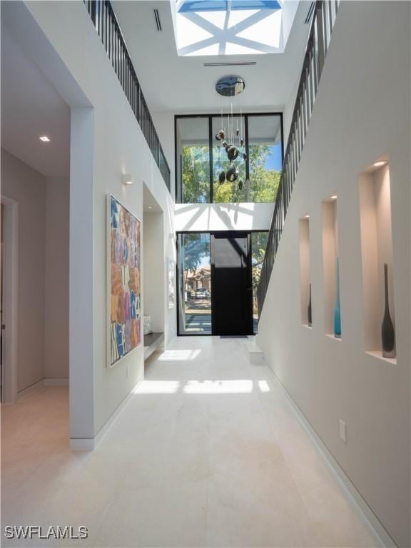 hall with a towering ceiling, visible vents, stairway, and baseboards