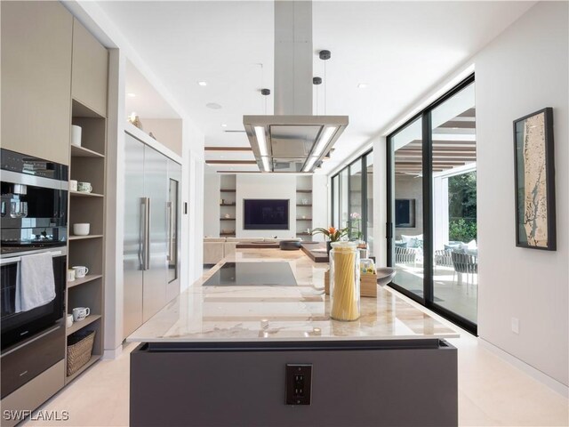 kitchen featuring stainless steel built in refrigerator, multiple ovens, a center island, a wall of windows, and light stone countertops