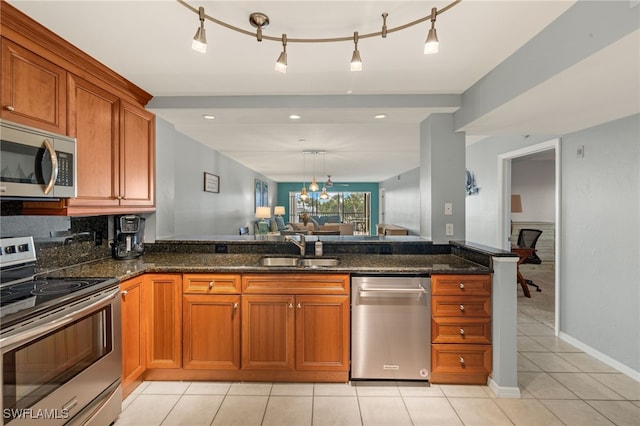 kitchen with rail lighting, sink, dark stone countertops, light tile patterned floors, and stainless steel appliances