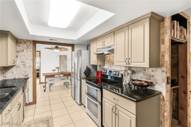 kitchen with stainless steel appliances, a raised ceiling, cream cabinets, and tasteful backsplash