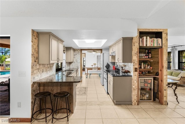 kitchen with a breakfast bar, a skylight, a sink, a peninsula, and stainless steel electric range