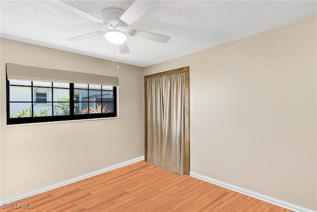 empty room with a textured ceiling, ceiling fan, light wood-style flooring, and baseboards