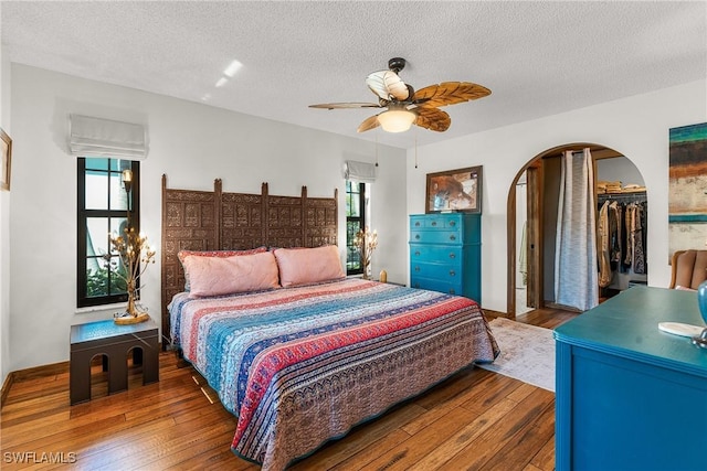 bedroom with arched walkways, multiple windows, and wood finished floors