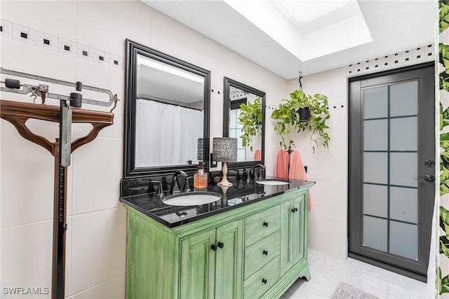 bathroom featuring double vanity, a skylight, tile walls, and a sink