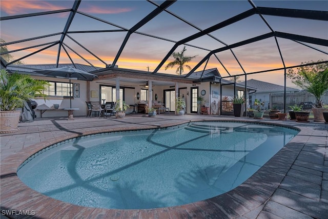 pool at dusk with ceiling fan, a patio area, and glass enclosure