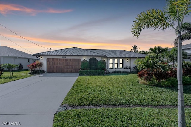 view of front of house featuring concrete driveway, metal roof, an attached garage, a yard, and stucco siding