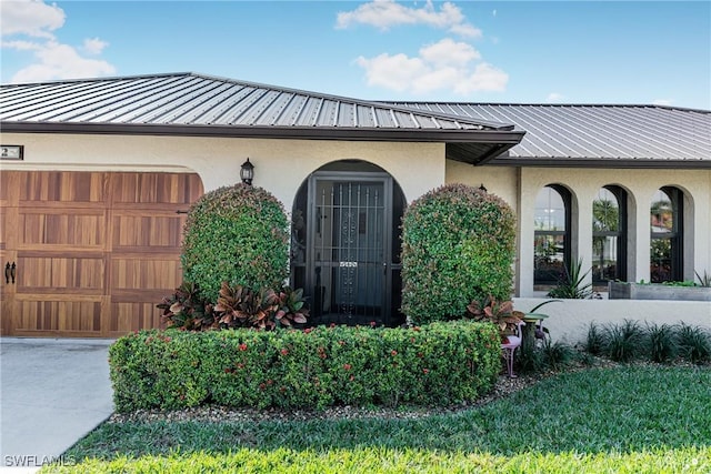 entrance to property featuring a garage, a standing seam roof, metal roof, and stucco siding