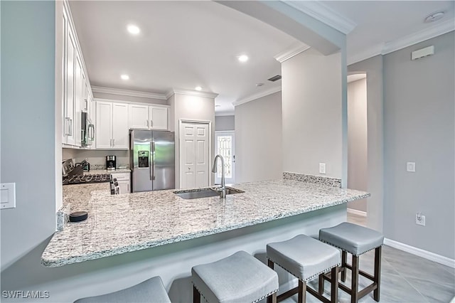 kitchen featuring a peninsula, a breakfast bar, stainless steel appliances, a sink, and white cabinetry