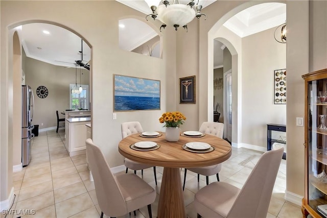 tiled dining space featuring crown molding, ceiling fan with notable chandelier, and a towering ceiling