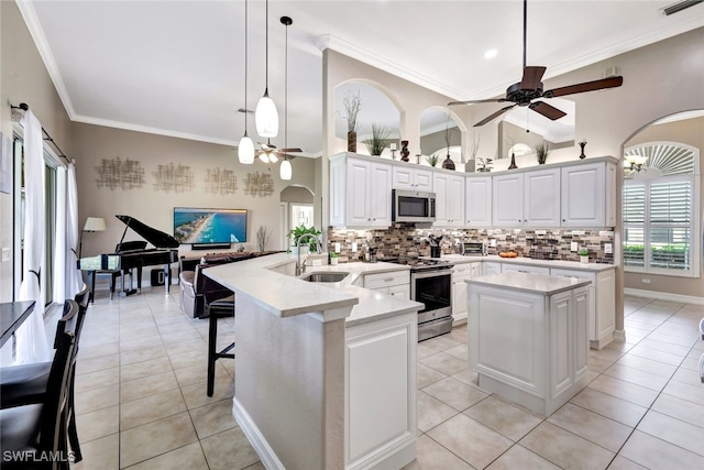 kitchen with sink, hanging light fixtures, a kitchen island, stainless steel appliances, and white cabinets