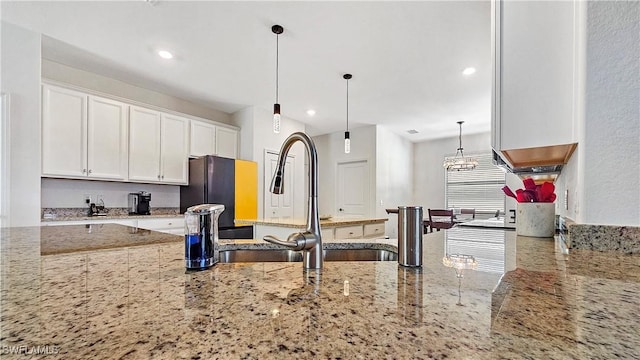 kitchen featuring black refrigerator, sink, white cabinets, hanging light fixtures, and light stone countertops