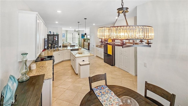 kitchen with light tile patterned flooring, decorative light fixtures, white cabinets, a center island, and light stone counters