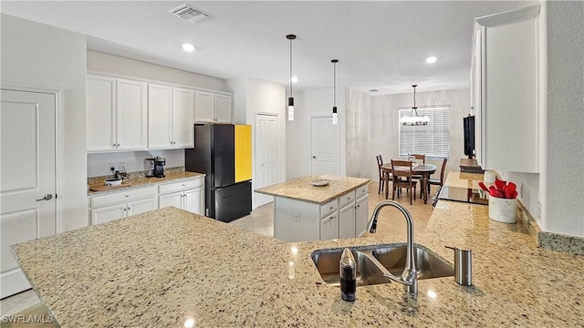 kitchen with white cabinetry, sink, black refrigerator, and a kitchen island