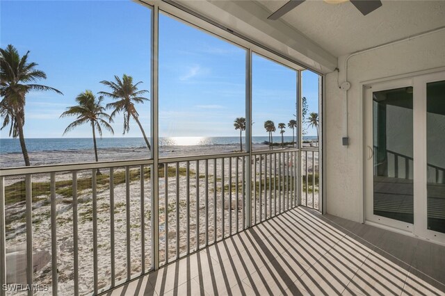 unfurnished sunroom featuring ceiling fan, a beach view, and a water view