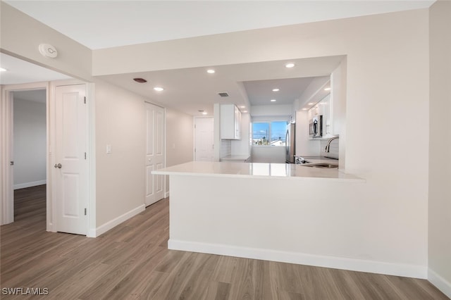 kitchen with a peninsula, baseboards, white cabinets, light countertops, and light wood-type flooring