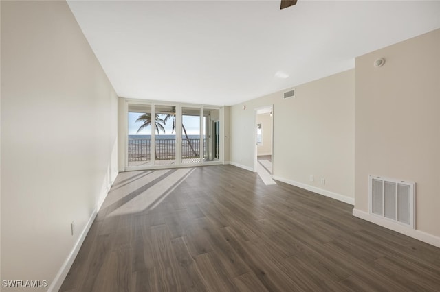 spare room featuring expansive windows, dark wood-style flooring, baseboards, and visible vents