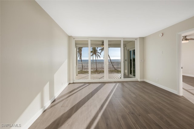 spare room with ceiling fan, expansive windows, baseboards, and wood finished floors