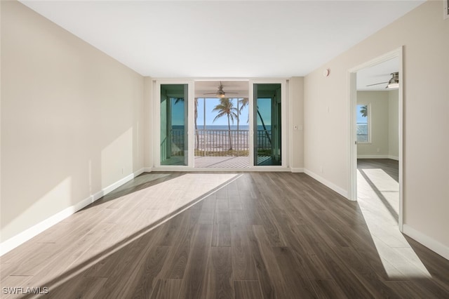 spare room with dark wood-style floors, floor to ceiling windows, visible vents, a ceiling fan, and baseboards