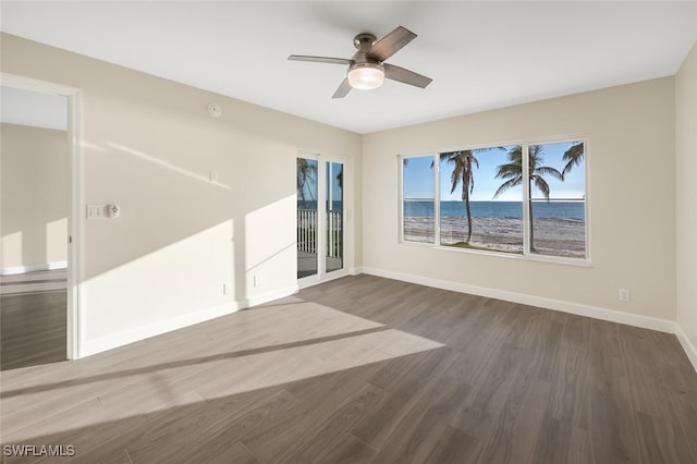 spare room featuring dark wood-type flooring, a water view, a ceiling fan, and baseboards