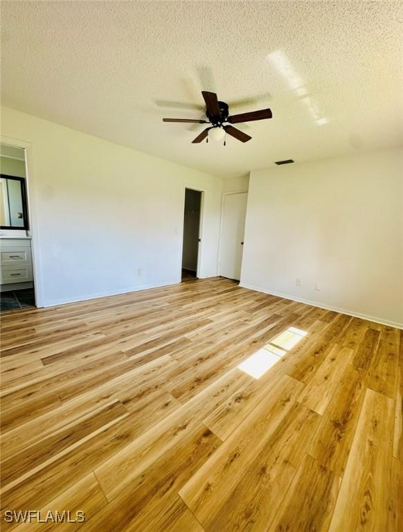 unfurnished bedroom with ceiling fan, ensuite bath, a textured ceiling, and light wood-type flooring