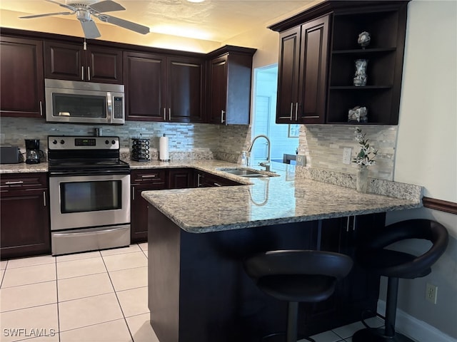 kitchen featuring light tile patterned flooring, stainless steel appliances, a peninsula, a sink, and a kitchen breakfast bar